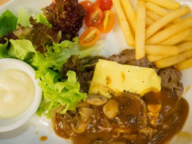 Peynirli ızgara biftek, yanında patates kızartması ve beyaz tabakta sebze.