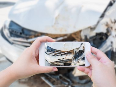 Cep telefonu kullanan bir kadın sigorta için araba kazası hasarının fotoğrafını çekiyor.