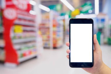 Kadın süpermarkette alışveriş yaparken cep telefonunu tutuyor. 