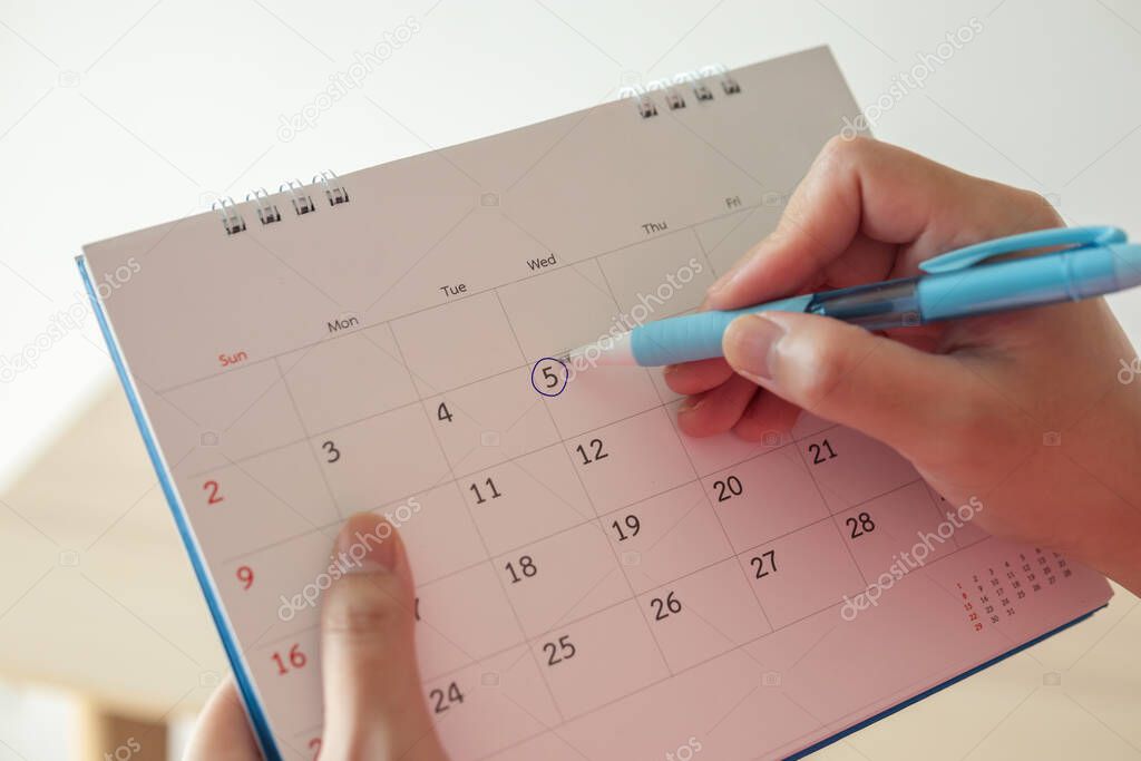 Hand with pen mark at 5th on calendar date with blue circle