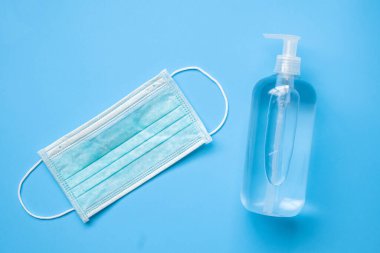 COVID-19 Coronavirus 'a karşı mavi arka planda cerrahi maske takılı alkol el dezenfektanı şişesi. Sağlık ve Tıp Konsepti