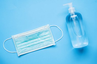 COVID-19 Coronavirus 'a karşı mavi arka planda cerrahi maske takılı alkol el dezenfektanı şişesi. Sağlık ve Tıp Konsepti