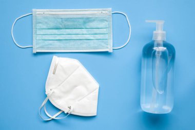 COVID-19 Coronavirus 'a karşı mavi arka plan korumalı KN95 cerrahi maske takılı alkollü el dezenfektanı şişesi. Sağlık ve Tıp Konsepti