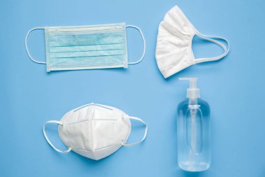 COVID-19 Coronavirus 'a karşı mavi arka plan korumalı KN95 cerrahi maske takılı alkollü el dezenfektanı şişesi. Sağlık ve Tıp Konsepti