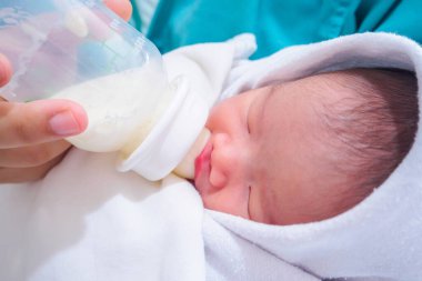 Anne yeni doğmuş bebeği şişeden besliyor.