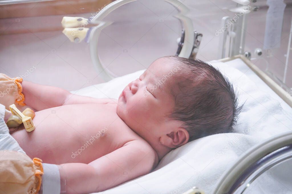 Newborn baby girl inside incubator in hospital post delivery room