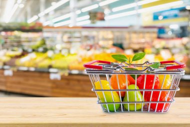 Marketin arka planında, ahşap masada meyveli alışveriş sepeti.