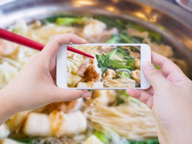 Kadın, Sukiyaki Shabu Shabu 'nun cep telefonuyla fotoğrafını çekiyor.