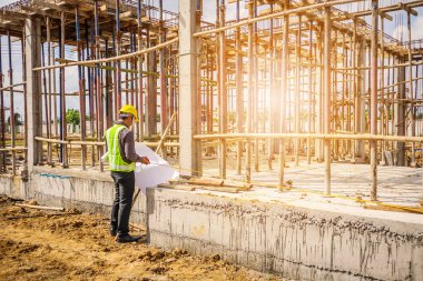 Asyalı işadamı inşaat mühendisi koruyucu miğfer ve bina inşaatının beton zeminini ölçen proje kağıtları.