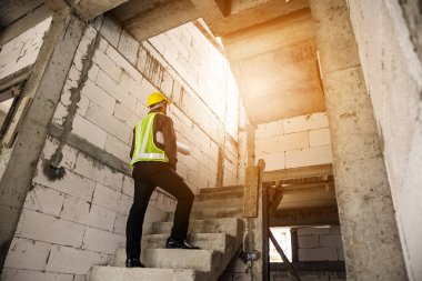 Genç profesyonel mühendis koruyucu miğfer ve bina şantiyesinde elinde proje kağıtları ile çalışıyor.