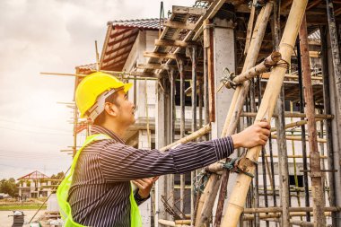 Genç profesyonel mühendis koruyucu miğfer ve bina inşaatında merdiven üzerinde çalışan planlar üzerinde çalışıyor.