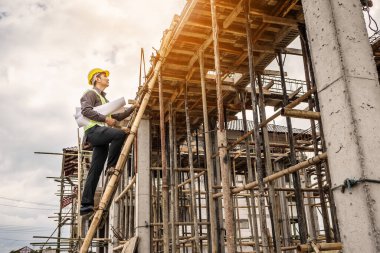 Genç profesyonel mühendis koruyucu miğfer ve bina inşaatında merdiven üzerinde çalışan planlar üzerinde çalışıyor.