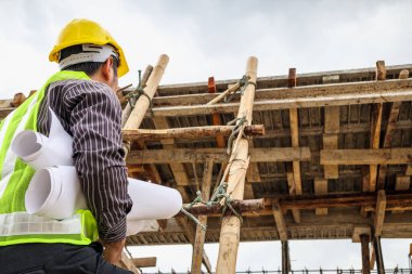 Genç profesyonel mühendis koruyucu miğfer ve bina inşaatında merdiven üzerinde çalışan planlar üzerinde çalışıyor.