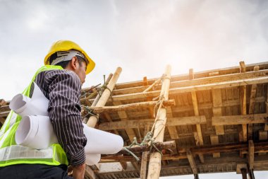 Genç profesyonel mühendis koruyucu miğfer ve bina inşaatında merdiven üzerinde çalışan planlar üzerinde çalışıyor.