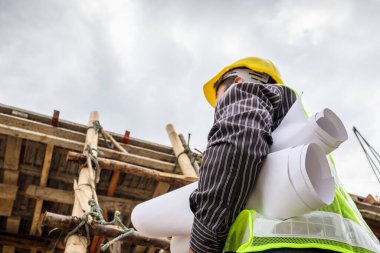 Genç profesyonel mühendis koruyucu miğfer ve bina inşaatında merdiven üzerinde çalışan planlar üzerinde çalışıyor.