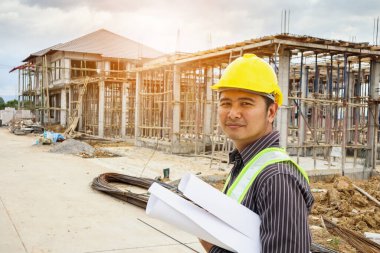 Asyalı işadamı inşaat mühendisi koruyucu miğfer ve bina inşaatında kullanılacak planlar.