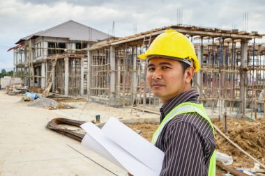 Asyalı işadamı inşaat mühendisi koruyucu miğfer ve bina inşaatında kullanılacak planlar.