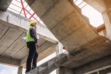 Genç profesyonel mühendis koruyucu miğfer ve bina şantiyesinde elinde proje kağıtları ile çalışıyor.