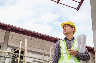 Asyalı işadamı inşaat mühendisi koruyucu miğfer ve bina inşaatında kullanılacak planlar.