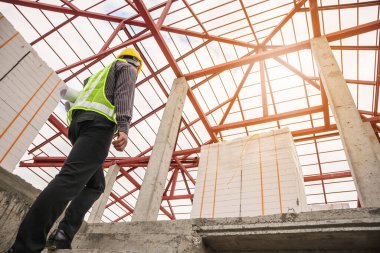 Genç profesyonel mühendis koruyucu miğfer ve bina şantiyesinde elinde proje kağıtları ile çalışıyor.