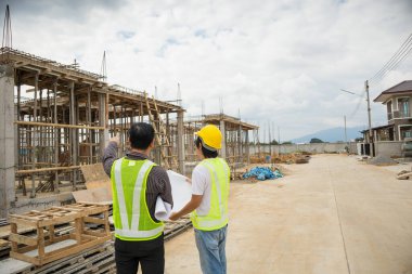 Asyalı işadamı inşaat müdürü ve koruyucu miğfer mühendisi bina inşaatında elinde planlar tutuyor.