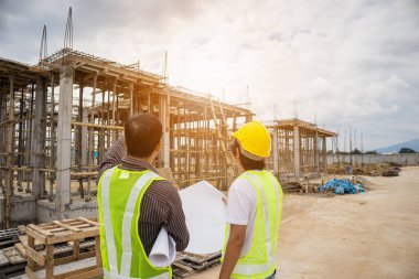 Asyalı işadamı inşaat müdürü ve koruyucu miğfer mühendisi bina inşaatında elinde planlar tutuyor.