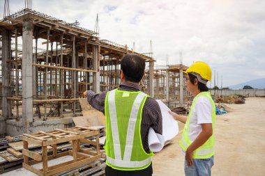 Asyalı işadamı inşaat müdürü ve koruyucu miğfer mühendisi bina inşaatında elinde planlar tutuyor.
