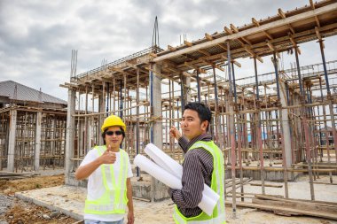 Asyalı işadamı inşaat müdürü ve koruyucu miğfer mühendisi bina inşaatında elinde planlar tutuyor.