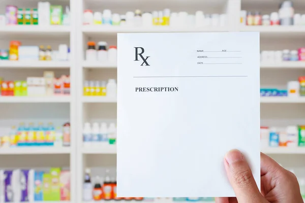 pharmacist hand holding prescription rx paper in hand over pharmacy store background