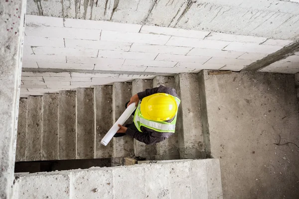 在房屋建筑工地手握防护头盔和蓝图纸的年轻专业工程师 — 图库照片