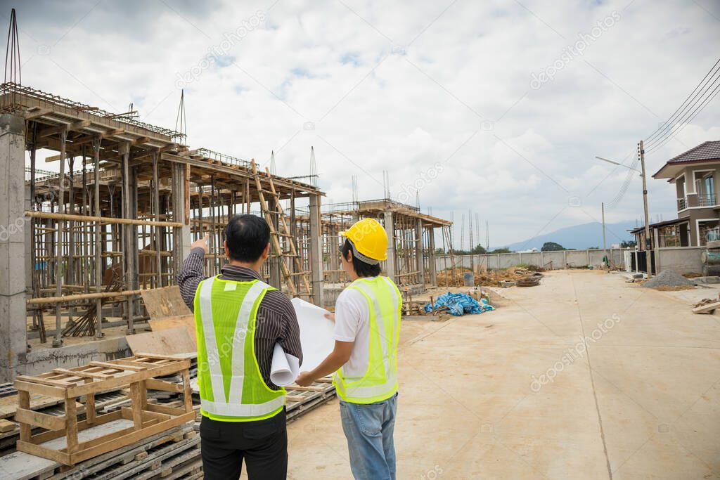 Asian business man construction manager and engineer worker in protective helmet hold blueprints paper on hand at house building site