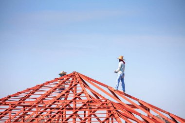 İnşaat işçileri binanın çatısının çelik iskelet yapısını inşa ediyorlar. İnşaat alanında bulutlar ve gökyüzü var.