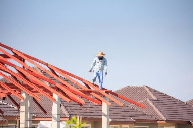 İnşaat işçileri binanın çatısının çelik iskelet yapısını inşa ediyorlar. İnşaat alanında bulutlar ve gökyüzü var.