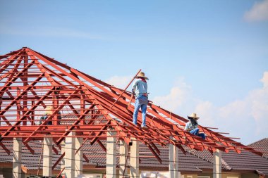 İnşaat işçileri binanın çatısının çelik iskelet yapısını inşa ediyorlar. İnşaat alanında bulutlar ve gökyüzü var.