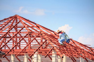 İnşaat işçileri binanın çatısının çelik iskelet yapısını inşa ediyorlar. İnşaat alanında bulutlar ve gökyüzü var.