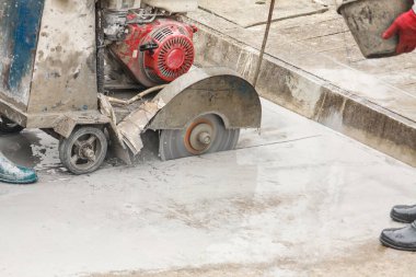 İnşaat alanında beton yol kesen elmas testeresi kullanan bir işçi.