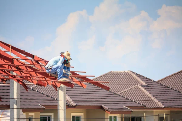 İnşaat işçileri binanın çatısının çelik iskelet yapısını inşa ediyorlar. İnşaat alanında bulutlar ve gökyüzü var.