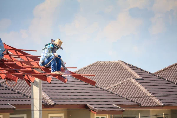 İnşaat işçileri binanın çatısının çelik iskelet yapısını inşa ediyorlar. İnşaat alanında bulutlar ve gökyüzü var.