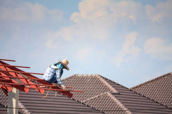 İnşaat işçileri binanın çatısının çelik iskelet yapısını inşa ediyorlar. İnşaat alanında bulutlar ve gökyüzü var.