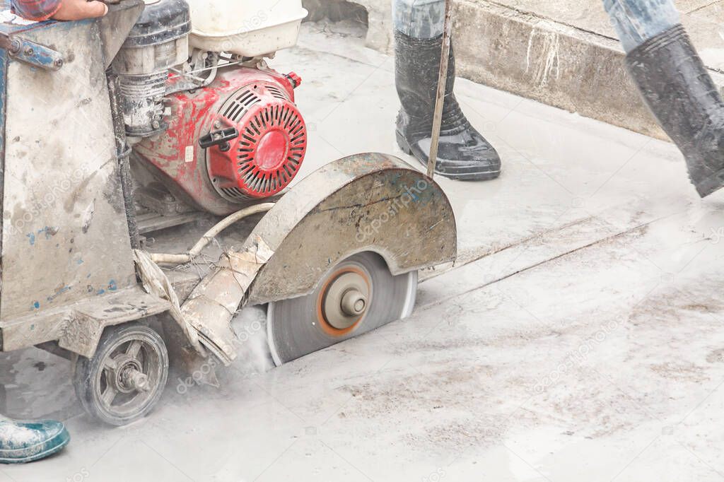 Worker using diamond saw blade machine cutting concrete road at construction site