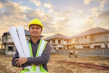 Asyalı işadamı inşaat mühendisi koruyucu miğfer ve bina inşaatında kullanılacak planlar.