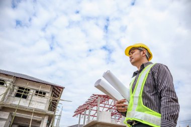 Asyalı işadamı inşaat mühendisi koruyucu miğfer ve bina inşaatında kullanılacak planlar.