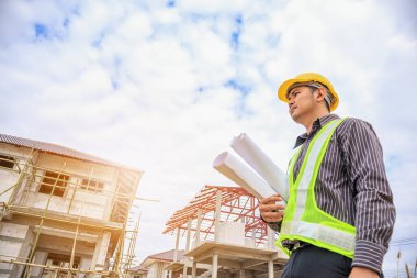 Asyalı işadamı inşaat mühendisi koruyucu miğfer ve bina inşaatında kullanılacak planlar.