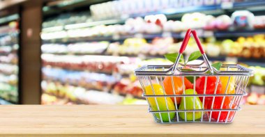 Marketin arka planında, ahşap masada meyveli alışveriş sepeti.