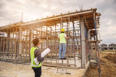 Asyalı işadamı inşaat müdürü ve koruyucu miğfer mühendisi inşaat alanının planlarını ellerinde tutuyorlar.