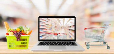 Süpermarket koridoru dizüstü bilgisayar ve alışveriş arabası ile bulanık arkaplan ahşap masa bakkalında online konsept