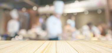 Boş ahşap masa üstü, aşçı restoranda yemek pişirirken arka planı bulanıklaşmış.