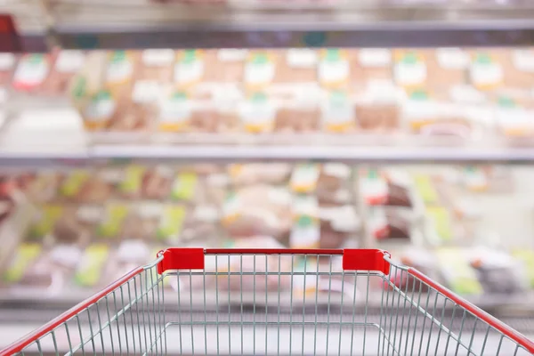 Empty red shopping cart with Abstract fresh meat shelves in supermarket grocery store blurred defocused background with bokeh light