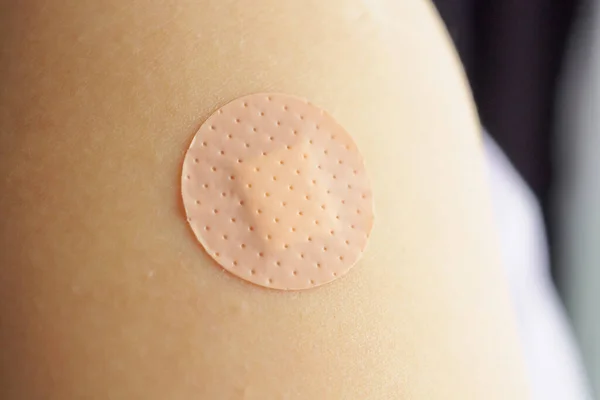 Close up circle brown adhesive bandage on patient arm after medicine injection or vaccination