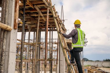 Genç profesyonel mühendis koruyucu miğfer ve bina inşaatında merdiven üzerinde çalışan planlar üzerinde çalışıyor.